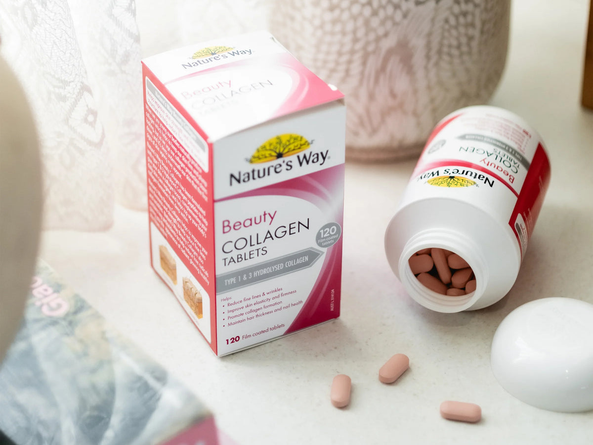 Nature's Way Beauty Collagen Tablets shown with its pink and white retail box, an open white bottle tipped on its side, several pink tablets scattered in front, and a white cap on a light countertop.